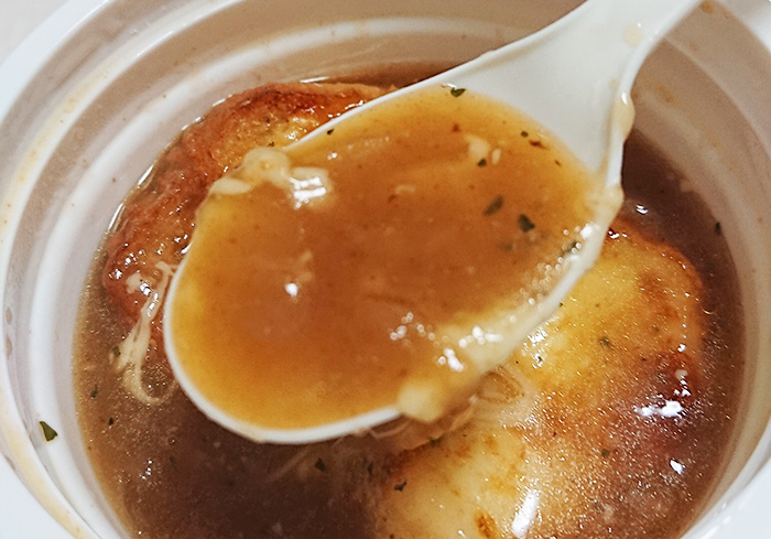 「こんがりチーズのオニオンスープ」のスープをスプーンですくった写真